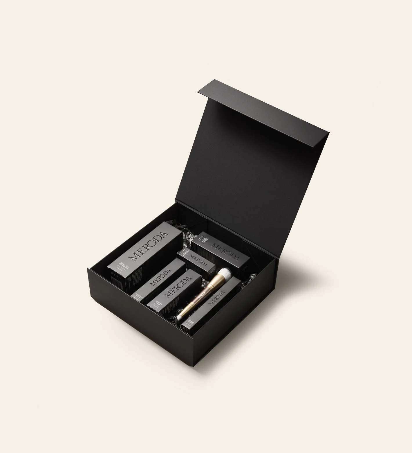 Matte black Gift Box with a magnetic closure filled with Meroda Cosmetics products and a gold makeup brush.