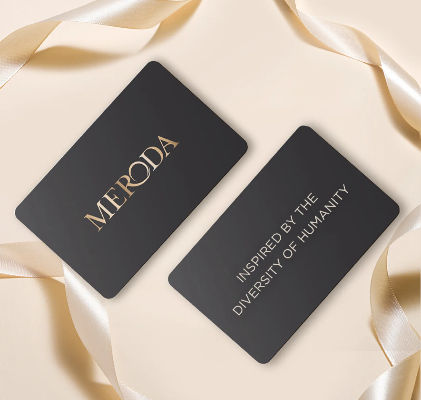 Meroda E-Gift Card featuring matte black cards with gold text and a cream satin ribbon on a light background.