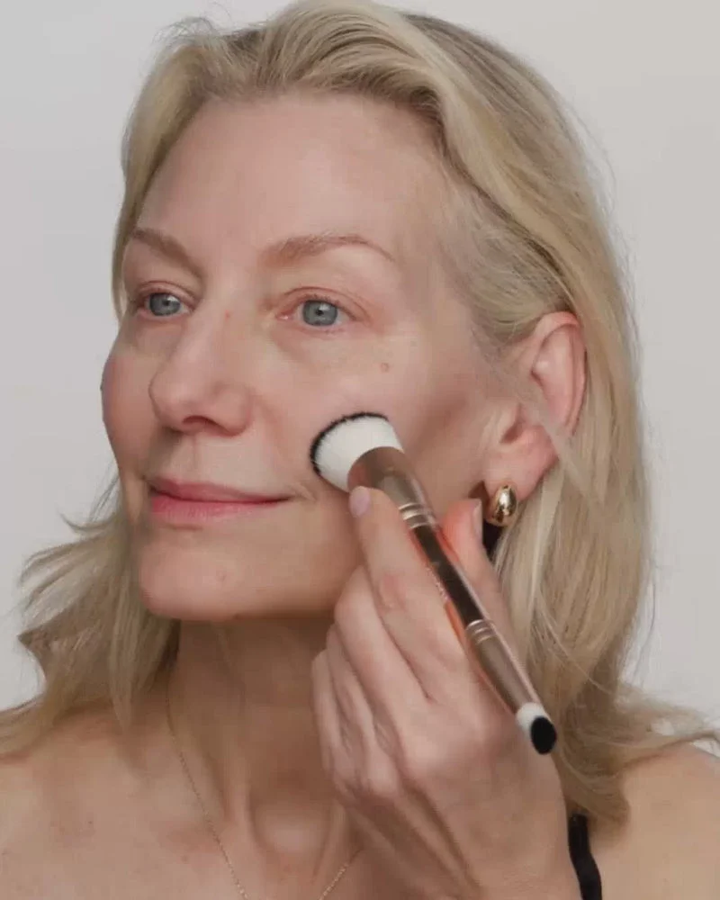 Mature woman blends Changing Foundation onto her face with a 2-in-1 brush for a fresh, even complexion.