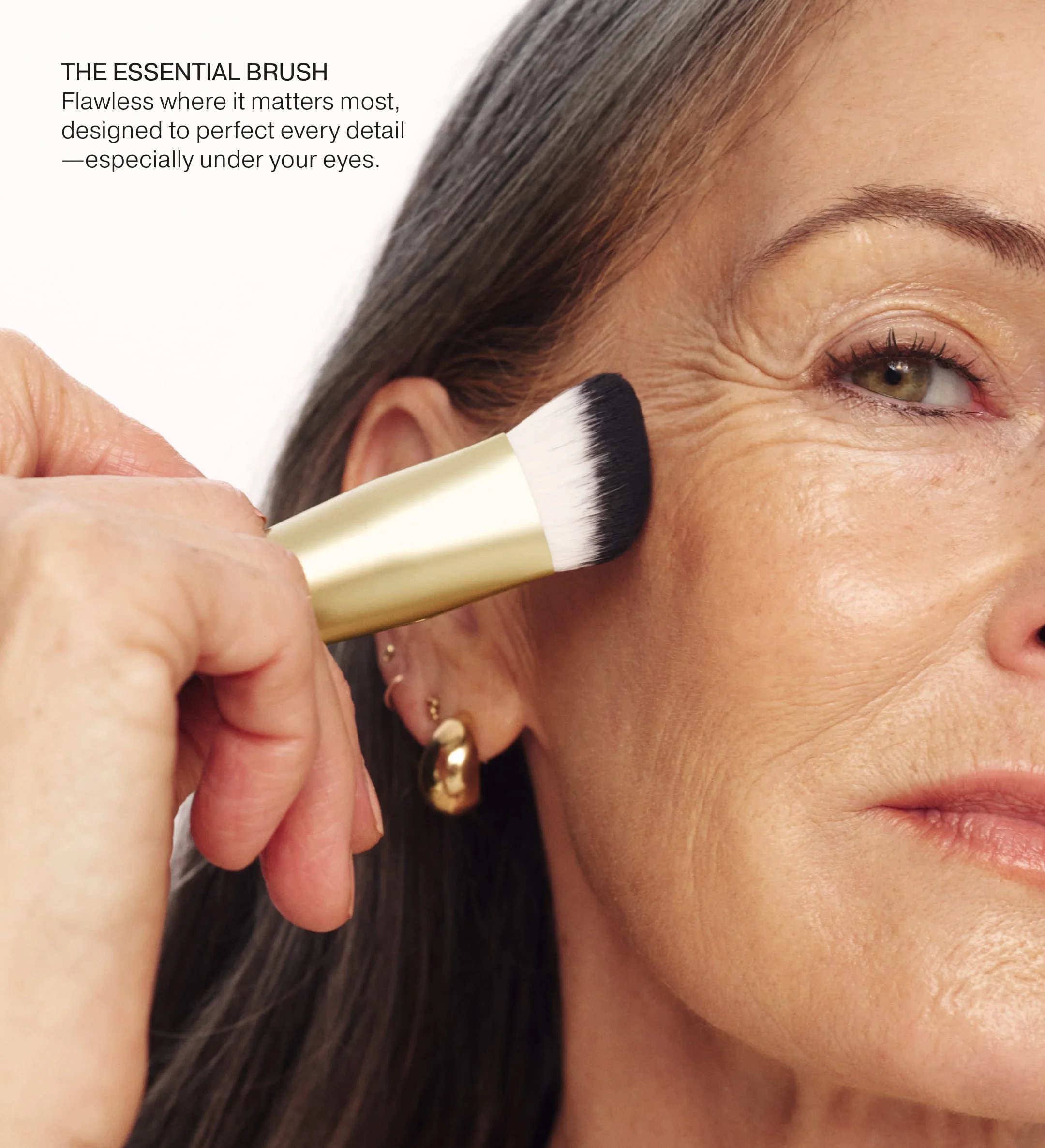 The Essential Brush with a gold handle blending makeup on a model for a seamless, flawless under-eye finish.