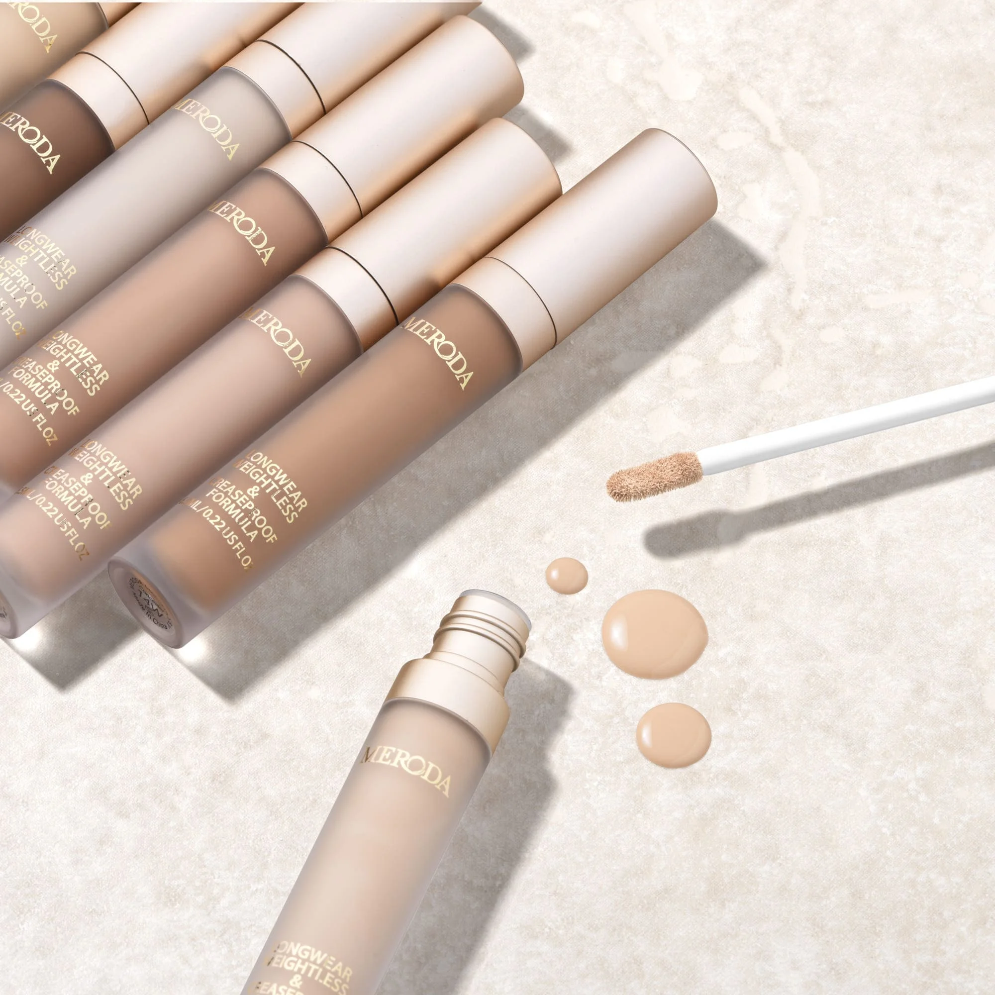 Universal Concealer in diverse shades with a creamy liquid texture and applicator on a light stone background.