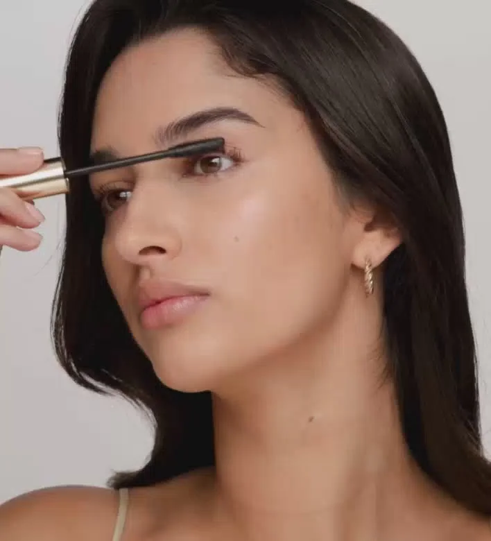 Applying Gilded Lashes Mascara with a gold-handled wand to create volumized, lengthened lashes.