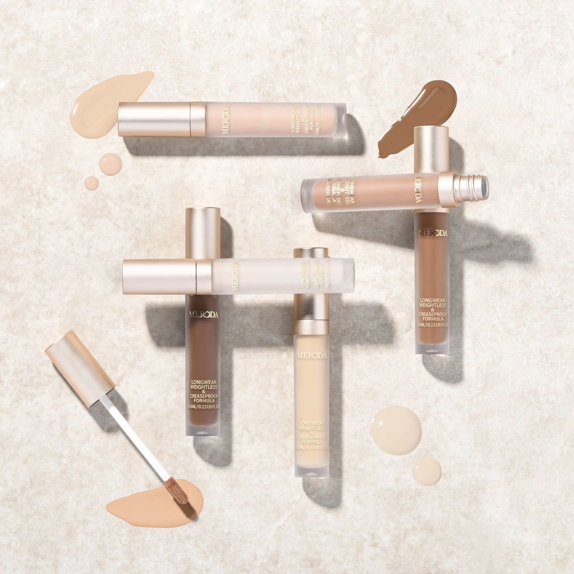 Meroda Universal Concealer tubes in various shades with liquid swatches and applicator wand on a light stone background.
