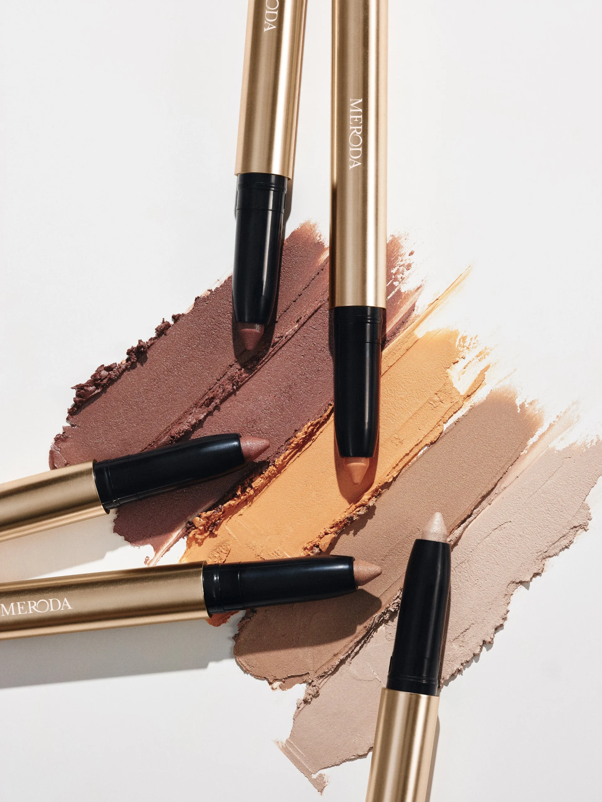Meroda Eye Perfecting Shimmer Stick swatches in shimmering Mauve, Gold, Champagne, Bronze, and Pearl.