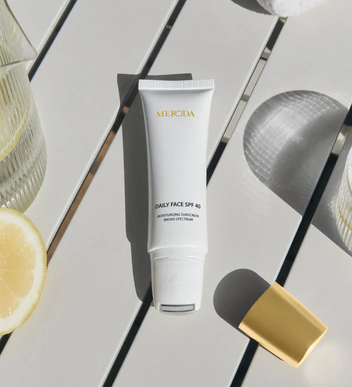 Daily Face SPF 40 tube with its cooling metal rollerball applicator on a bright table with a fresh lemon slice.