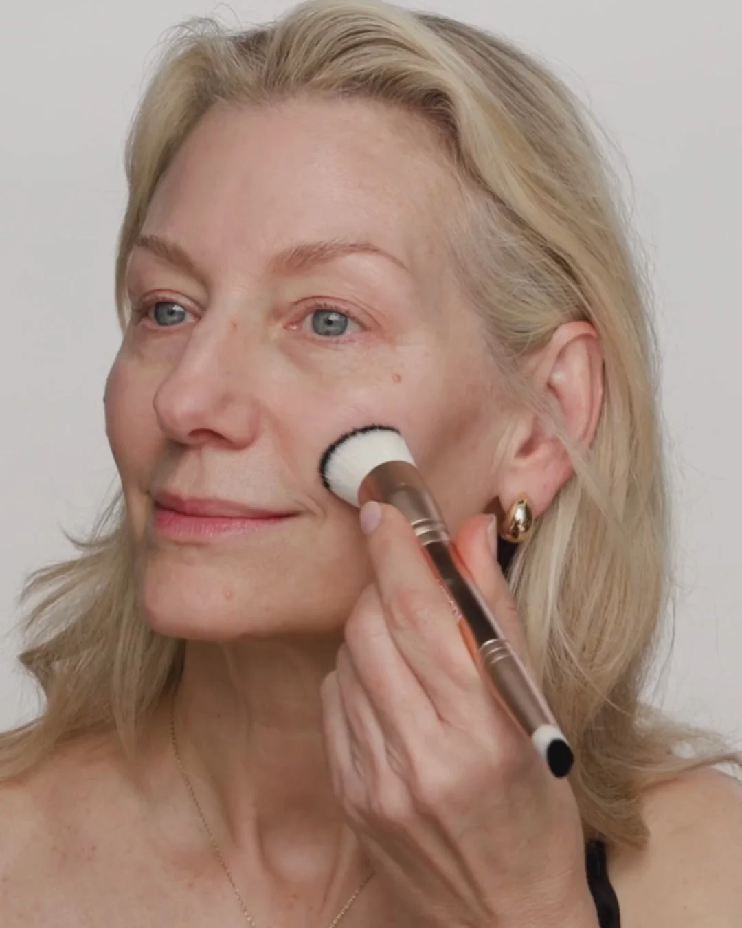 Mature woman blending Changing Foundation with a 2-in-1 Build & Conceal Brush for a seamless, natural glow.