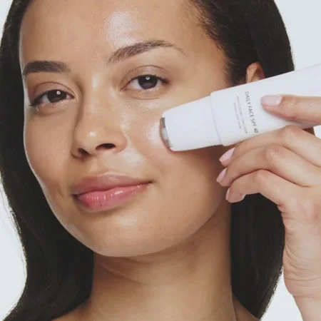 Daily Face SPF 40 applied with a cooling metal rollerball to a woman's cheek for a hydrated, glowing finish.