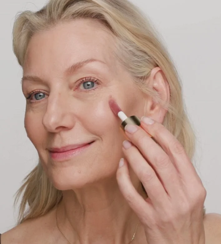 Model applying Mini Liquid Blush in Dusty Rose on cheeks using a makeup brush for a natural look.
